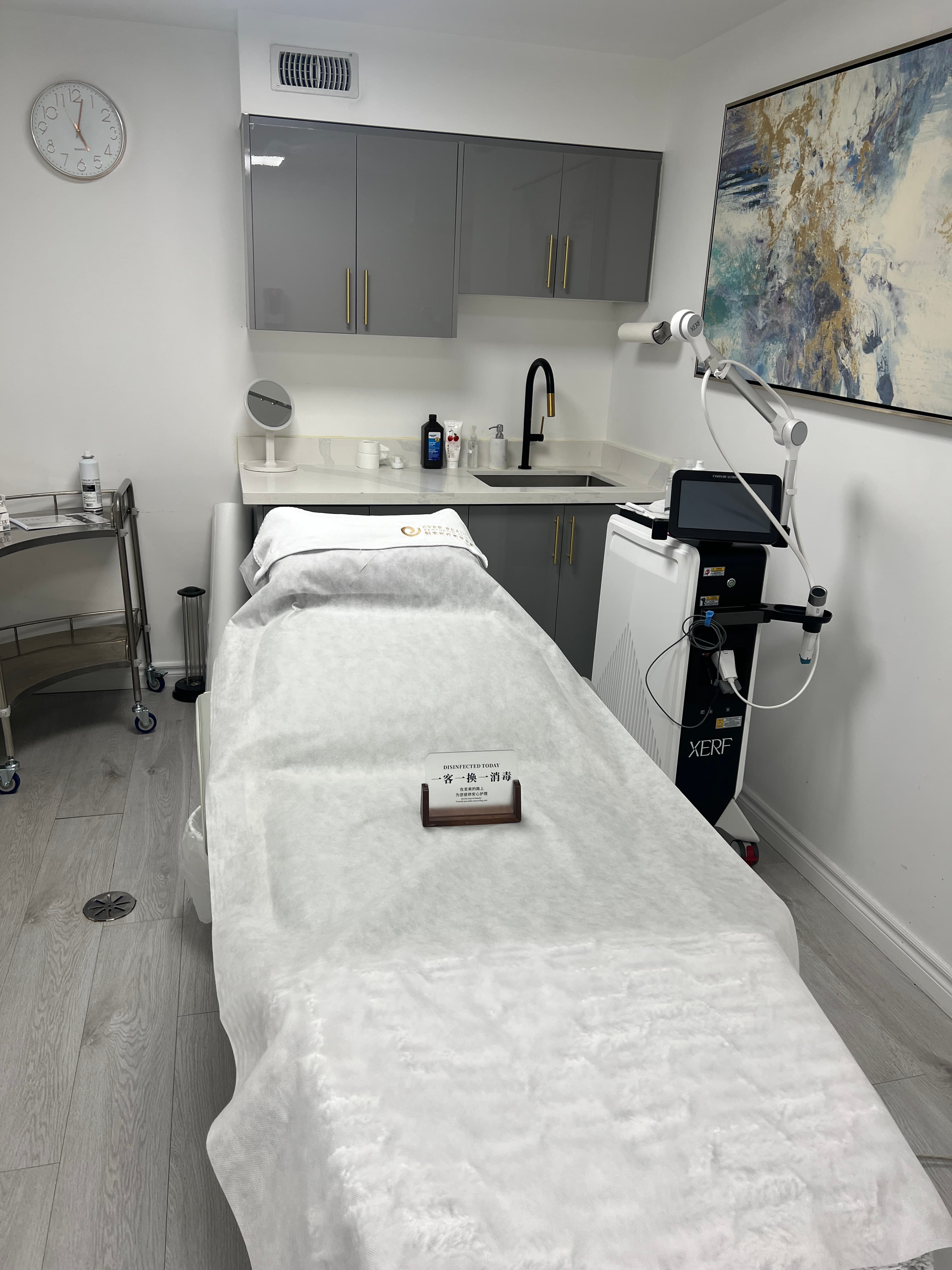 Modern aesthetic room with a white treatment bed, XERF laser machine, and grey cabinets.