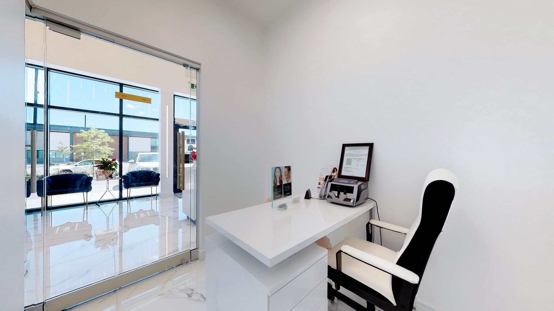 Modern white desk and ergonomic chair in a bright, minimalist office with marble-patterned floors.