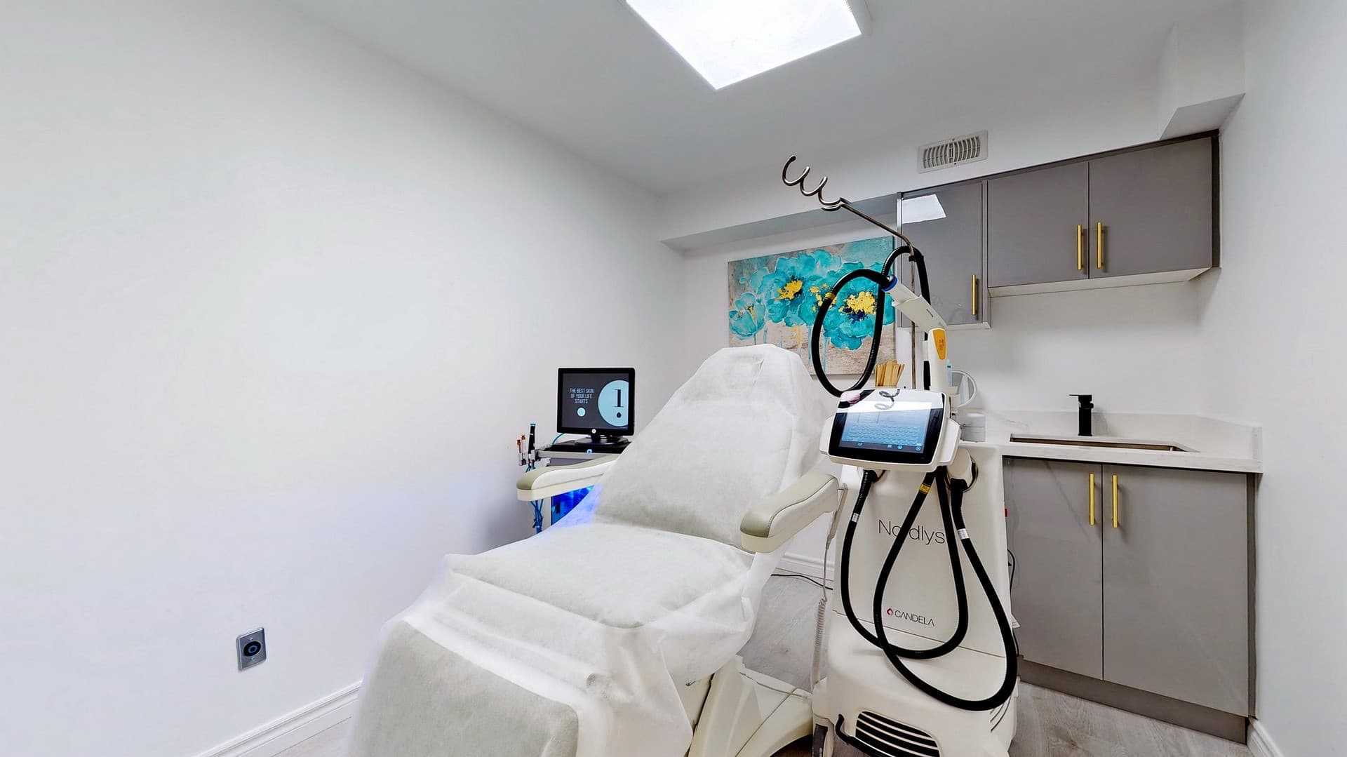 Bright aesthetic room with a white treatment bed, Nordlys laser machine, and grey cabinetry.